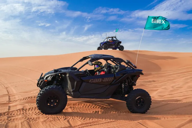 Black Can-Am Maverick X3 on a dune crest with a SAND X flag