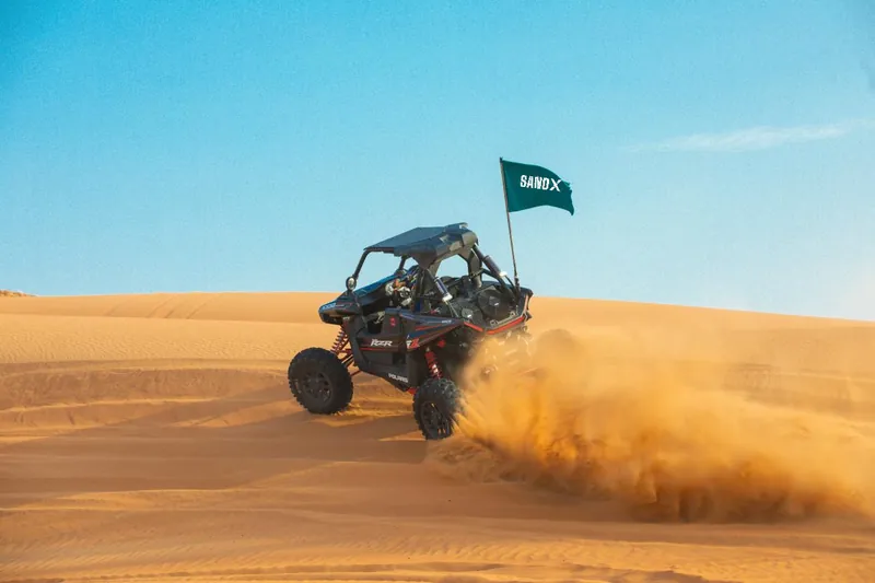 Polaris RZR RS1 throwing a plume of sand under a blue sky