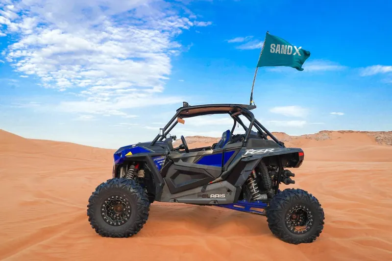Blue Polaris RZR Turbo S two-seat buggy on orange sand with a SAND X flag
