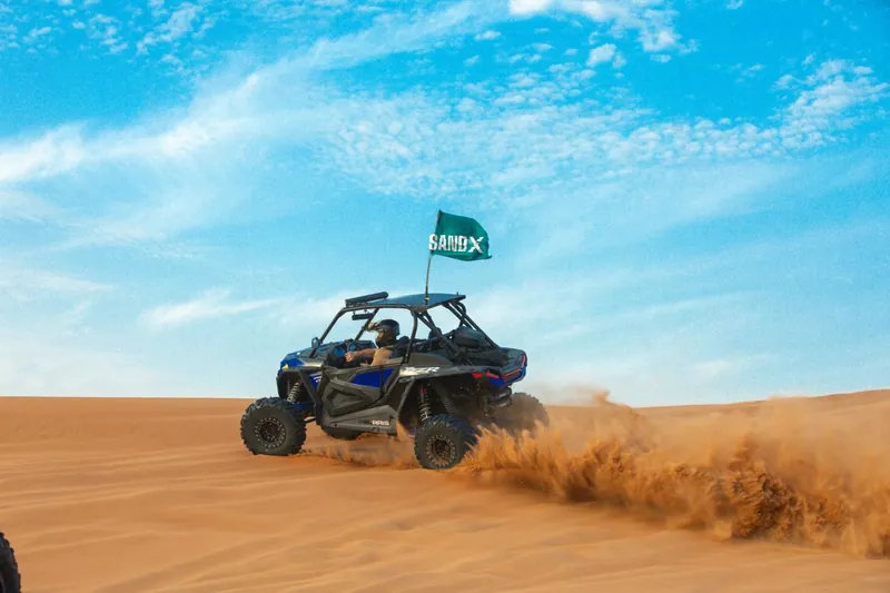 Blue Polaris RZR Turbo S kicking up sand under a blue sky
